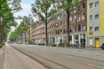 Casa envelhecida exterior contra estrada e bicicletas estacionadas entre árvores cobertas durante o dia em Amsterdam Holland — Fotografia de Stock