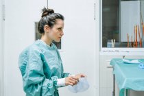 Jovem cirurgiã veterinária feminina em uniforme verde colocando tampa descartável enquanto olha para a frente na clínica — Fotografia de Stock