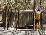 Vista posteriore del bambino irriconoscibile in piedi sulla veranda del cottage moderno situato nel bosco in estate mentre piange triste — Foto stock