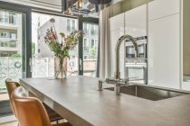 Elegante interno di cucina moderna con armadi bianchi ed elettrodomestici e lavandino nel bancone sopra il bancone in grande casa con parete di vetro — Foto stock