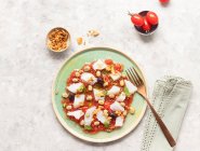 Insalata estiva di pomodoro e merluzzo in un piatto poco profondo con una forchetta e una ciotola di cipolle fritte — Foto stock