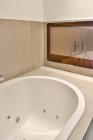 Деталь білої керамічної ванни, розташованої в сучасній ванній кімнаті з бежевими стінами — стокове фото