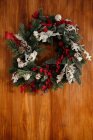 Elegante corona di Natale con ramoscelli di conifere ed elementi decorativi appesi alla parete di legno alla luce del giorno — Foto stock