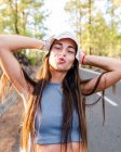 Adolescente femenina sincera con el pelo largo y las manos detrás de la cabeza mirando a la cámara en un día soleado en Tenerife España - foto de stock