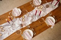 De cima de toalha de mesa branca e placas colocadas na mesa festiva decorada com velas ardentes e galhos secos de árvore — Fotografia de Stock