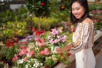Giovane acquirente femminile etnica sincera selezionando fiori fioriti con piacevole profumo nel negozio in giardino durante il giorno — Foto stock