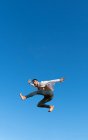 De baixo vista lateral do atleta enérgico no desgaste da moda realizando truque contra o céu azul na luz solar — Fotografia de Stock