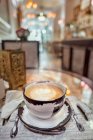 Keramische Tasse aromatischen Kaffees mit Latte Art auf dem Tisch mit Servietten und blühenden Rosen in der Cafeteria — Stockfoto