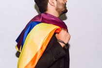 Ritaglia irriconoscibile barbuto maschio giocare e sventolare bandiera multicolore simbolo di orgoglio LGBTQ — Foto stock