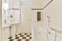 Design criativo do banheiro com lâmpada entre lavatórios contra banho em forma retangular no piso de azulejos em casa — Fotografia de Stock