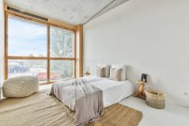 Креативный дизайн спальни с подушками и чехлом на кровати на полу дома у окна — стоковое фото