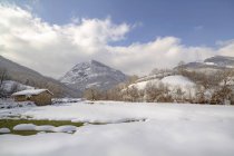Paisagem paisagística de encostas de montanha e vale coberto por neve branca com pequena casa rural sob céu azul nublado em Redes Parque Natural localizado em Caleão Astúrias Espanha — Fotografia de Stock