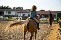 Back view of anonymous female with male trainer riding stallions in countryside on sunny day — Stock Photo