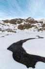 Пейзаж сніжного схилу пагорба в високогір'ї під хмарним небом вдень і річкою крижаної води — стокове фото
