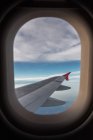 Через окно самолета вид на пушистые облака над морем и местность в дневное время — стоковое фото