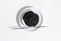 Зверху керамічна миска з смачною спагетті з чорним кальмаром з паличками на білому тлі — стокове фото