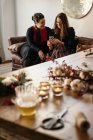 Positive women friends sitting on sofa and laughing while browsing smartphone in room with Christmas decorations in daytime — Stock Photo