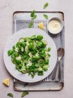 Vista superior da deliciosa salada verde com pedaços de pepino fresco e folhas de espinafre com sementes de gergelim preto contra molho de limão — Fotografia de Stock