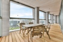 Balcone interno con tavolo e poltrone in legno contro finestre e colonne sotto soffitto a casa — Foto stock