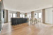 Intérieur élégant d'une zone de cuisine spacieuse avec mobilier noir et table en bois dans un appartement contemporain en journée — Photo de stock