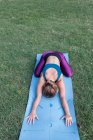 D'en haut de jeune femme méconnaissable en vêtements de sport étirement tout en pratiquant le yoga sur tapis sur l'herbe verte dans le parc à la lumière du jour — Photo de stock