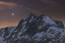 Scenic view of dark mounts with snow and rough peaks under starry sky at dusk — Stock Photo