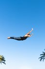 Снизу вид энергичного спортсмена в модной одежде, выполняющего трюк против голубого неба под солнечным светом — стоковое фото