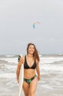 Молодая веселая спортсменка с летящими волосами и доской для серфинга в океане с пеной под облачным небом — стоковое фото