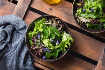 Von oben schmackhafter vegetarischer Salat mit grünen und roten Salatblättern und essbaren Blüten gegen Ölkrug — Stockfoto