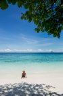 Back view turista donna in costume da bagno e cappello di paglia seduta in mare trasparente durante il viaggio in Malesia — Foto stock