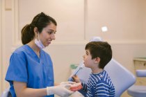 Жіночий ортодонт навчає пацієнта зубною щіткою чистити зуби за моделлю щелепи в стоматологічній клініці. — стокове фото