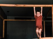 Positives kleines Kind hängt auf hölzernem Himmelbett, während es im Schlafzimmer Spaß hat und in die Kamera schaut — Stockfoto