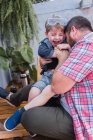 Неузнаваемый бородатый отец в клетчатой рубашке играет с веселым мальчиком в защитных очках, сидя днем — стоковое фото