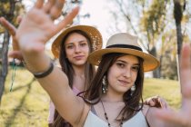 Content female teenagers with outstretched arms interacting while looking at camera on meadow in summer — Stock Photo