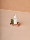 Small white bottle of cosmetic serum placed on stacked brown marble stone pieces on fabric on beige background — Stock Photo