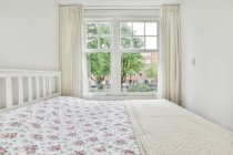 Interior minimalista do quarto com cama confortável contra janelas e paredes claras durante o dia — Fotografia de Stock
