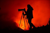Seitenansicht der Silhouette einer Frau, die mit Teleobjektiv und Stativ die Lavaexplosion auf La Palma Kanarische Inseln 2021 fotografiert — Stockfoto