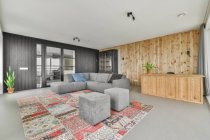 Серый диван размещен на красочном ковре в гостиной с деревянными стенами в современной квартире — стоковое фото