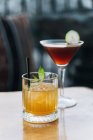 Bicchiere di cristallo di whisky cocktail con cubetti di ghiaccio e foglie di menta e vetro Manhattan con fetta di lime — Foto stock