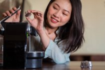 Ernte lächelnde junge ethnische Frau legt Kaffeepads in Kaffeemaschine auf den Tisch in Hausküche — Stockfoto