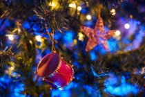 Decorative drum shaped toys hanging on branches of coniferous Christmas tree with glowing shiny garland — Stock Photo