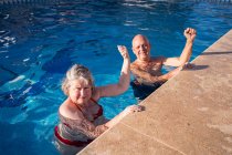 Alto ángulo de pareja mayor en traje de baño con los puños levantados nadando en la piscina azul limpia - foto de stock