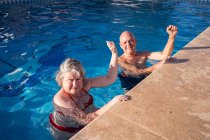 High angle of senior couple in swimwear with raised fists up swimming in clean blue pool — Stock Photo