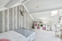 Interno bianco di camera da letto moderna con comodo letto e toeletta in legno situato in soffitta di casa — Foto stock