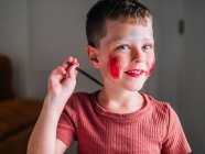 Charmante enfant avec applicateur de maquillage regardant la caméra à la table avec palette de fards à paupières — Photo de stock