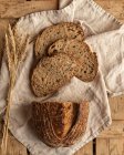 Vista dall'alto di pezzi di pane fresco di cereali con punte di grano su tessuto increspato su superficie di legno — Foto stock