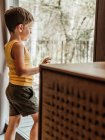 Мовчазна дитина стоїть біля вікна в котеджі і дивиться в думки — стокове фото