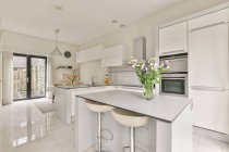 Cucina moderna con sedie e tavolo contro costruito in elettrodomestici e porta di vetro in casa luce — Foto stock