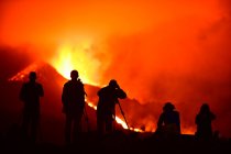 Людські силуети стоять і фотографують з триногами вибухову лаву на Канарських островах 2021 року, а два сидячих силуети спостерігають за природним явищем.. — стокове фото
