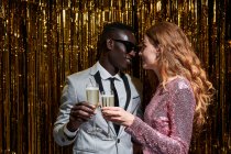 Cosecha sincera joven mujer abrazando elegante novio negro mientras tintineo copas de champán durante la celebración de Nochevieja - foto de stock